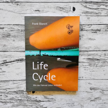 Auf dem Bild ist das Buch Life Cycle von Frank Glanert auf einer hellen, holzähnlichen Fläche abgebildet. Es dient als Headerbild für die Rezension.