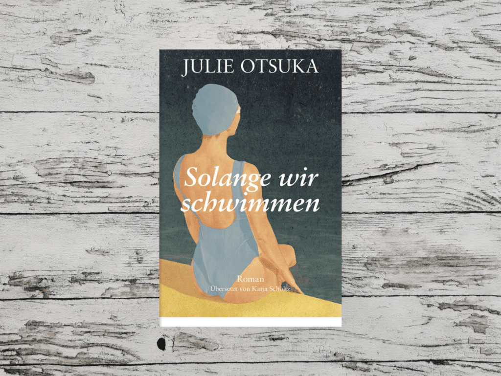 Auf dem Bild ist das Buchcover von "Solange wir schwimmen" von Julie Otsuka auf einer hellen, holzähnlichen Oberfläche. Das Bild ist das Headerbild für den Beitrag, der eine Rezension des Buchs enthält.