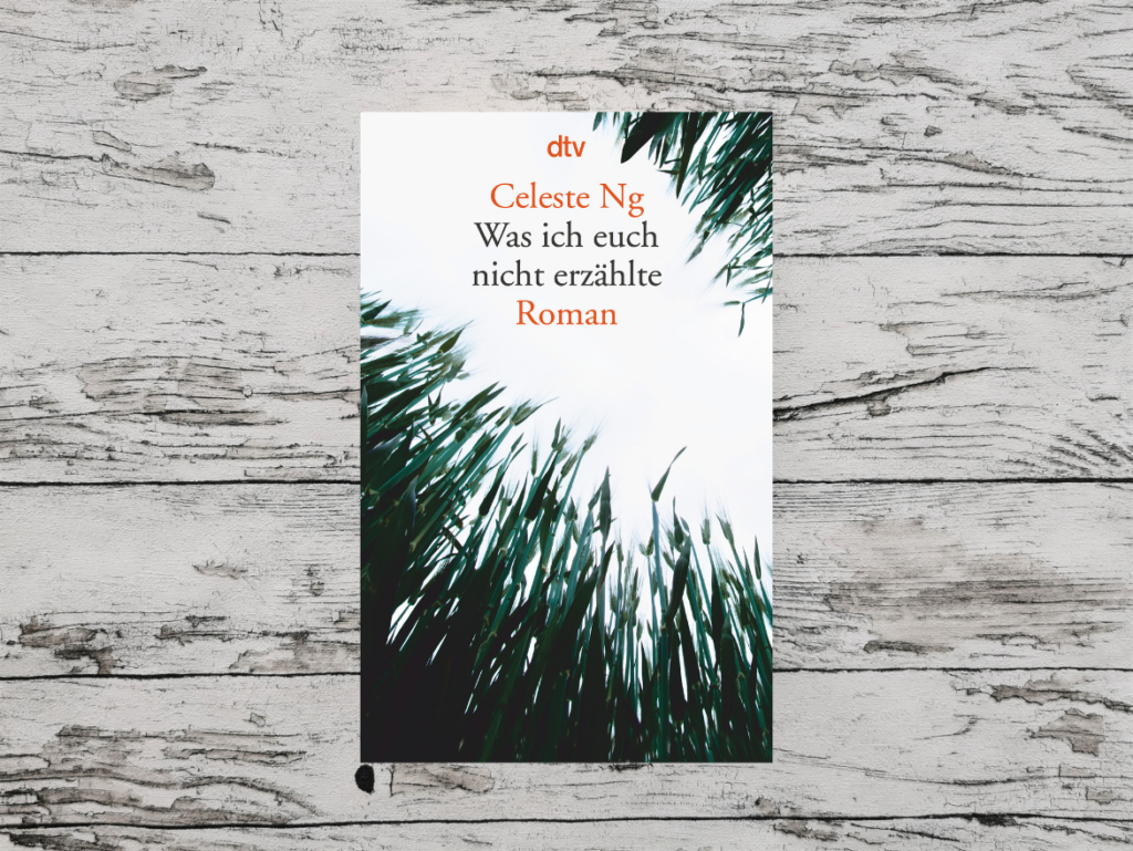 Auf dem Foto ist das Buchcover des Romans "Was ich euch nicht erzählte" von Celeste Ng auf einer hellen, holzähnlichen Oberfläche zu sehen.