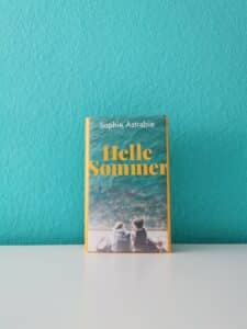Auf dem Bild ist das Buch "Helle Sommer" von Sophie Astrabie an eine türkise Wand gelehnt abgebildet. Es geht im Text um das Buch.