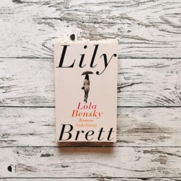 Auf dem Bild ist das Buch Lola Bensky von Lily Brett auf einer hellen, holzähnlichen Fläche abgebildet. Es ist das Headerbild zur Rezension des Buchs.