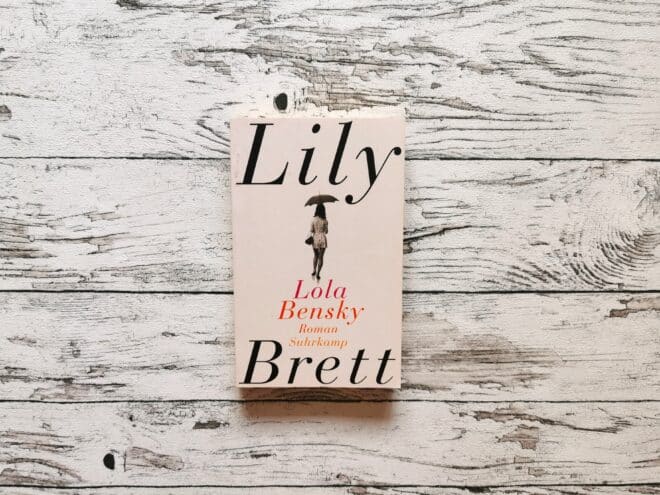 Auf dem Bild ist das Buch Lola Bensky von Lily Brett auf einer hellen, holzähnlichen Fläche abgebildet. Es ist das Headerbild zur Rezension des Buchs.