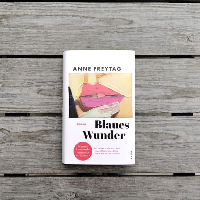 Auf dem Foto ist das Buch Blaues Wunder von Anne Freytag auf einem gräulichen Holzgartentisch abgebildet. Es ist das Headerbild zur Rezension des Buchs.