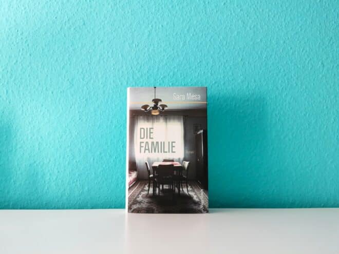 Auf dem Foto ist das Buch Die Familie von Sara Mesa auf einer weißen Fläche stehend vor einer türkisen Wand abgebildet. Es ist das Header-Bild zur Rezension des Buchs.