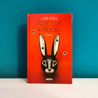 Auf dem Foto ist das Buch Wie die Karnickel von Jasper Fforde vor einer dunkelgrünen Wand auf einer glatten weißen Fläche stehend abgebildet. Es ist das Header-Bild meiner Rezension des Buchs.