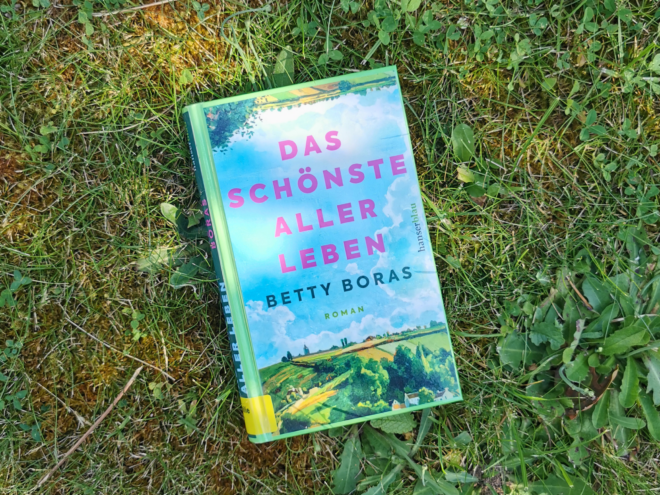 Das Buch Das schönste aller Leben von Betty Boras liegt auf einer Wiese. Es ist das Header-Bild für eine Rezension des Buchs.