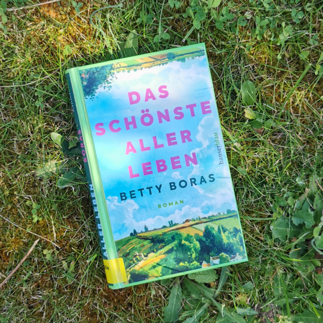 Das Buch Das schönste aller Leben von Betty Boras liegt auf einer Wiese. Es ist das Header-Bild für eine Rezension des Buchs.