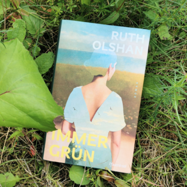 Das Buch Immergrün von Ruth Olshan umgeben von Pflanzen. Es ist das Headerbild zu einer Rezension des Buches.