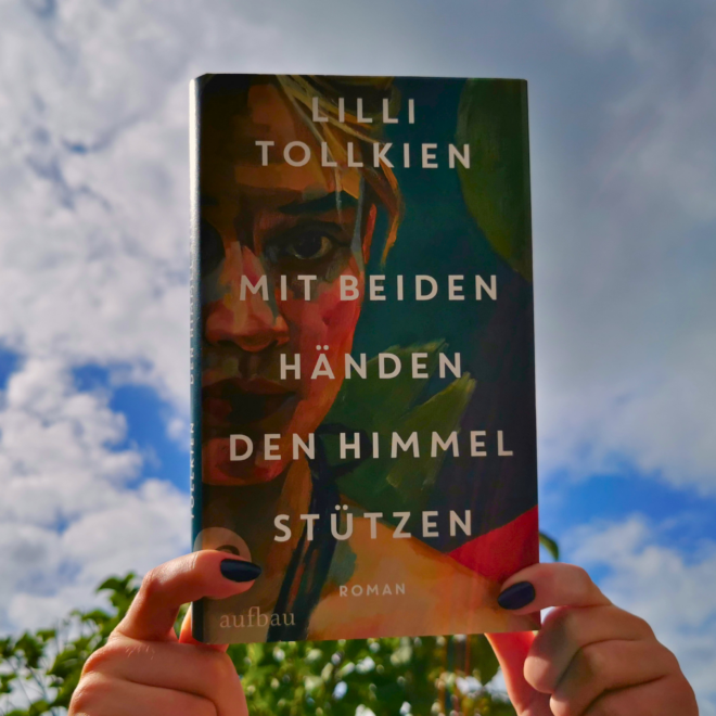 Zwei Hände mit dunkelblau lackierten Nägeln halten das Buch »Mit beiden Händen den Himmel stützen« von Lilli Tollkien gegen einen blauen Himmel mit weißen Wolken; am unteren Bildrand grüne Blätter. Das Cover zeigt in malerischem Stil ein Frauengesicht in warmen Erd-, Rot- und Grüntönen.