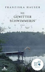 Buchcover „Die Gewitterschwimmerin" von Franziska Hauser, Roman, Eichborn. Ein düsterer Waldsee mit Steg, von dem eine nackte Person kopfüber ins Wasser springt; auf der Wasseroberfläche Regentropfen. Runder Störer: „2018 deutscher buchpreis – Nominiert".