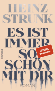 Buchcover „Es ist immer so schön mit dir" von Heinz Strunk, Roman, Rowohlt. Zarter beiger Hintergrund, Titel in großen dunkelblauen Serifenlettern, die nach unten zu verlaufen bzw. zu zerfließen scheinen; roter Aufkleber „SPIEGEL Bestseller".