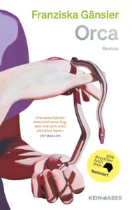 Buchcover „Orca" von Franziska Gänsler, Roman, Kein & Aber. Vor violettem Hintergrund halten zwei blasse Hände eine dunkelrote, glänzende, aalartige Form. Runder gelber Störer: „2026 deutscher buchpreis – Shortlist".